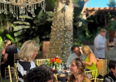 Guests mingling at an elegant outdoor garden party with crystal chandelier, string lights, and gold chairs.