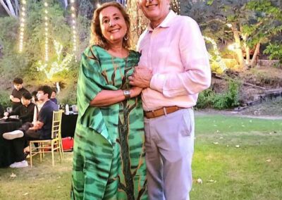 Elegant couple embraces at outdoor evening event with string lights and trees, woman in green tree-print gown.