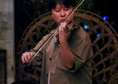 Man in olive jacket playing violin with eyes closed at an intimate evening venue with ornate metal decor