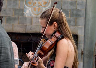 Young woman with long blonde hair playing violin outdoors near a decorative tiled wall