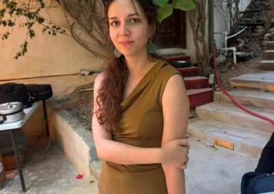 Woman in olive dress with sunglasses on head standing outdoors near stone steps and greenery on sunny day