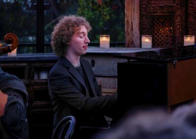 Young pianist with curly hair playing piano at intimate candlelit evening concert in cozy wooden venue setting