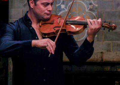 Man in black shirt playing violin with focused expression against decorative tiled wall backdrop