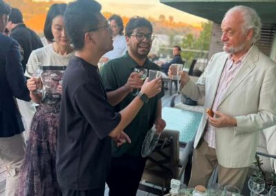 Guests toasting drinks at outdoor rooftop cocktail party during golden hour sunset with pool and hillside views