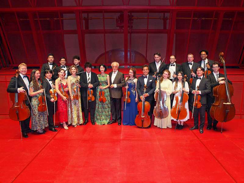 Carlsbad concert. Chamber orchestra ensemble in formal attire posing with string instruments on red stage after concert performance