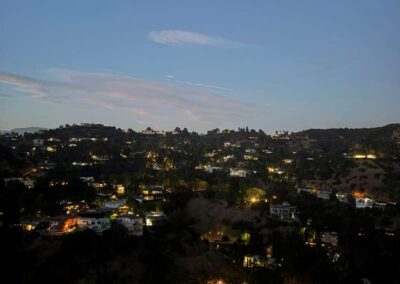 Twilight view of hillside homes with glowing lights nestled among trees under a gradient blue and pink sky.