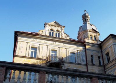Weathered historic building with ornate facade, decorative gable, domed tower, and balcony against clear blue sky with moon