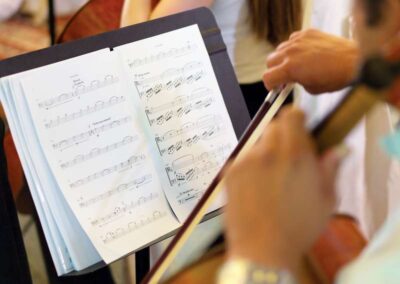 Musician playing string instrument with bow while reading sheet music on a black stand during rehearsal or performance