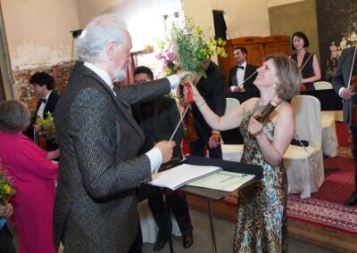 Conductor receiving flowers from smiling woman in leopard-print dress after classical music concert performance