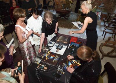 Author signing books and CDs at indoor event while fans gather around table to purchase merchandise.