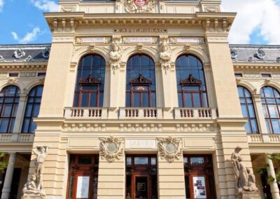Historic Kaiser-Bad spa building in Karlovy Vary with ornate facade, statues, and blooming pink roses in foreground
