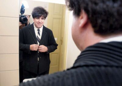Man in dark suit and striped tie buttoning jacket while looking at his reflection in a mirror