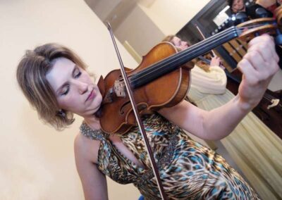 Woman in leopard-print dress playing violin with eyes closed at an indoor musical performance or recital.