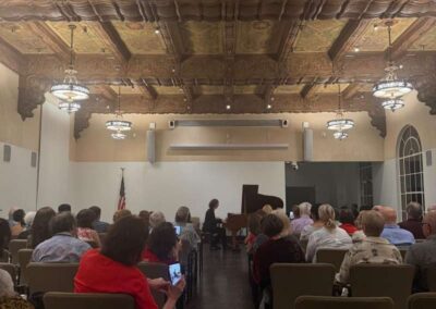 Audience seated in ornate historic hall watching pianist perform at intimate classical music concert under decorative ceiling.