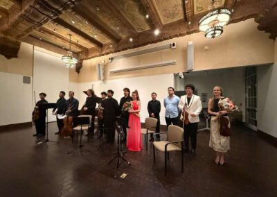 Chamber music ensemble taking a bow on stage in an ornate concert hall with musicians holding instruments and bouquets