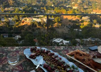 Elegant appetizer platter with olives and canapés on outdoor table overlooking Hollywood Hills at sunset.