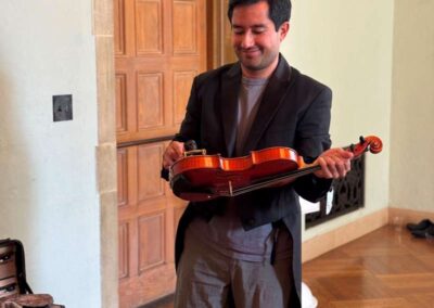 Smiling man in dark blazer holding a violin in an elegant room with wooden doors and parquet flooring.