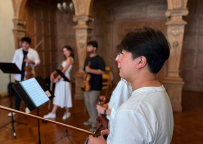 String quartet musicians rehearsing with violins and sheet music in an ornate wood-paneled hall with arches.