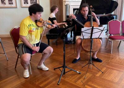 Piano trio rehearsing with violin, cello, and grand piano in an elegant gallery room with music stands and parquet floor.