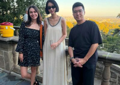 Three friends posing together on a scenic hilltop terrace at sunset with a city skyline view in the background.