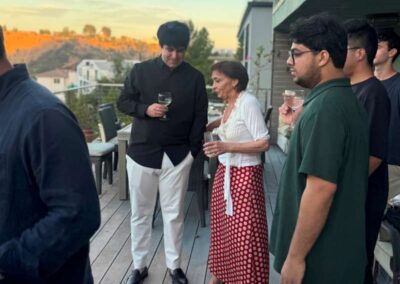 Group of people socializing with drinks on an outdoor deck at sunset overlooking hills and homes.
